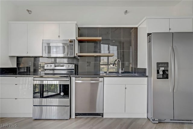 kitchen with stainless steel appliances, dark countertops, light wood-style flooring, and tasteful backsplash