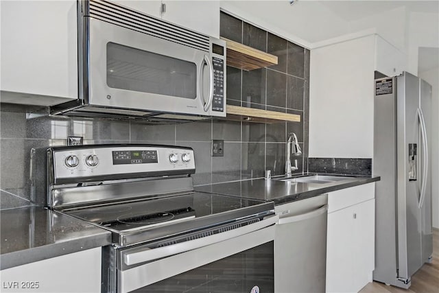 kitchen with stainless steel appliances, open shelves, a sink, dark countertops, and white cabinetry