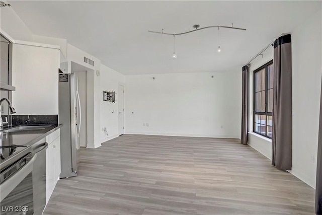 kitchen with a sink, appliances with stainless steel finishes, dark countertops, and light wood-style flooring
