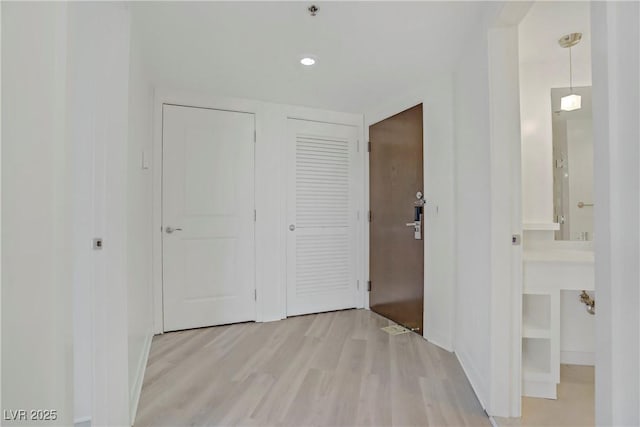 hallway featuring light wood-style flooring, baseboards, and recessed lighting