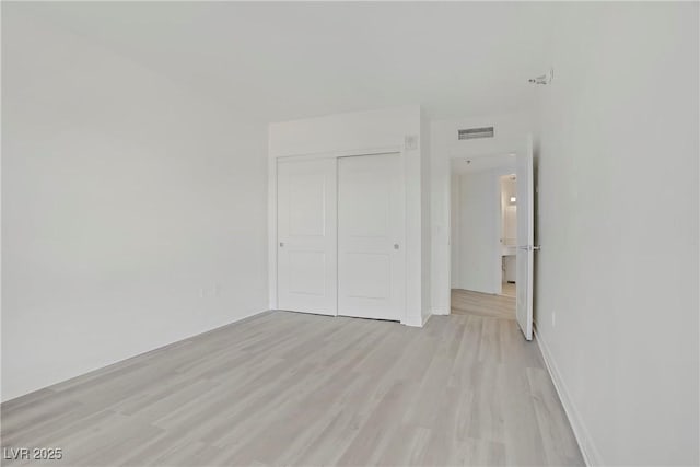 unfurnished bedroom featuring light wood-type flooring, a closet, and baseboards