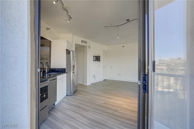 kitchen featuring stainless steel appliances, dark countertops, light wood-type flooring, and white cabinetry