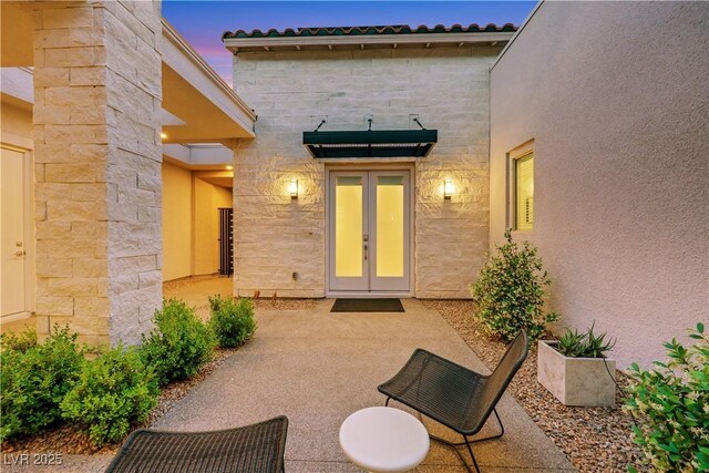 11895 Skyline Arch Ct, Las Vegas, NV 89138 - exterior entry at dusk featuring a patio area, stone siding, a tiled roof, french doors, and stucco siding
