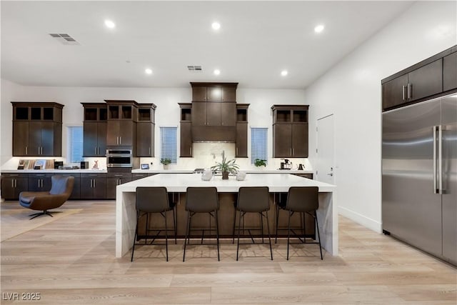 11895 Skyline Arch Ct, Las Vegas, NV 89138 - kitchen with stainless steel appliances, a large island, light countertops, dark brown cabinets, and light wood-type flooring