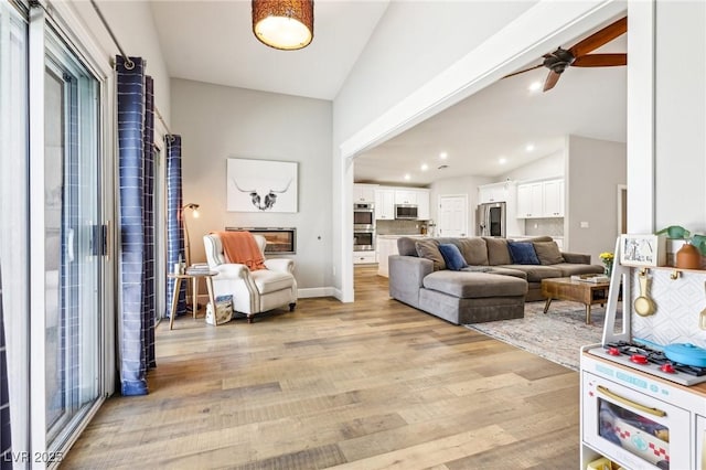 living room featuring light wood-style flooring, ceiling fan, high vaulted ceiling, and recessed lighting