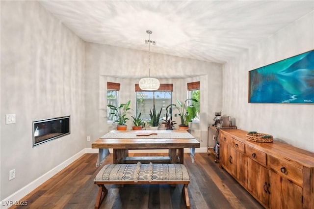 dining area featuring dark wood-type flooring, baseboards, and a glass covered fireplace