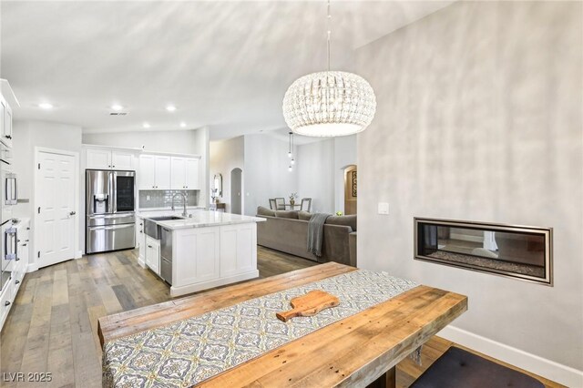 kitchen with stainless steel refrigerator with ice dispenser, arched walkways, a sink, light wood-type flooring, and white cabinetry