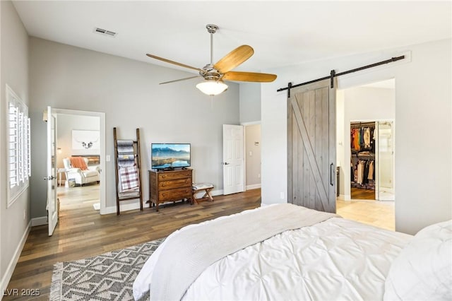 bedroom with a barn door, high vaulted ceiling, wood finished floors, baseboards, and a walk in closet
