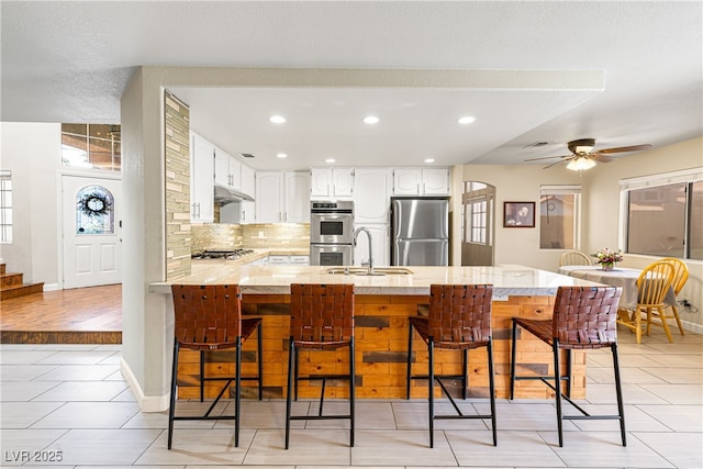 5449 Desert Spring Rd, Las Vegas, NV 89149 - kitchen with appliances with stainless steel finishes, a peninsula, under cabinet range hood, a sink, and a breakfast bar area