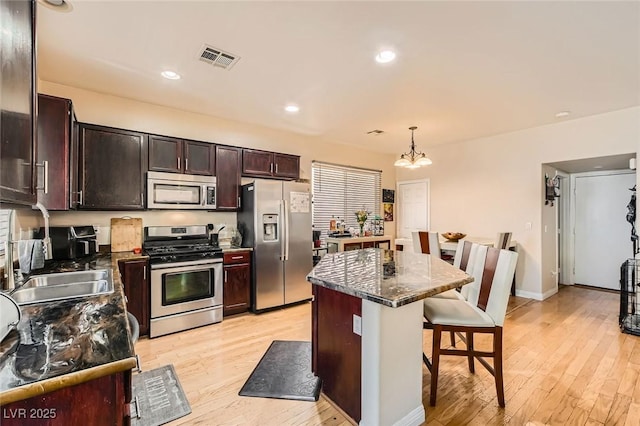 kitchen featuring stainless steel appliances, a breakfast bar, light wood-type flooring, a chandelier, and recessed lighting