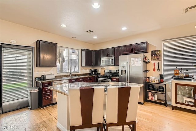 kitchen with appliances with stainless steel finishes, light wood finished floors, a kitchen island, a sink, and stone countertops