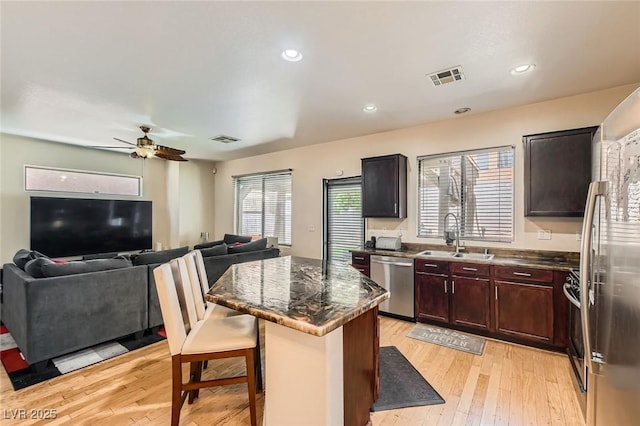 kitchen with stainless steel appliances, a sink, ceiling fan, light wood-style floors, and a kitchen island