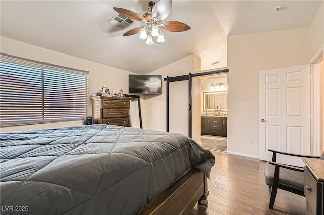 bedroom with vaulted ceiling, wood finished floors, a barn door, ensuite bath, and ceiling fan