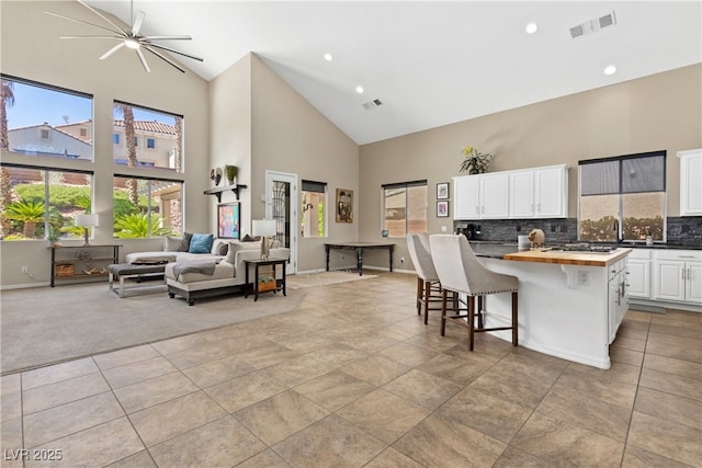 kitchen with high vaulted ceiling, wood counters, healthy amount of natural light, white cabinetry, and open floor plan
