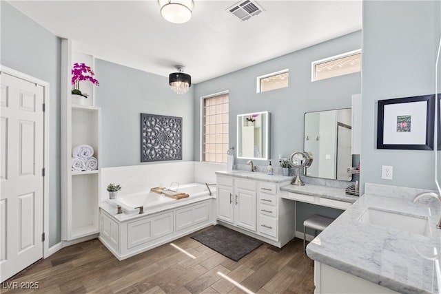 bathroom with two vanities, wood finished floors, a garden tub, and walk in shower