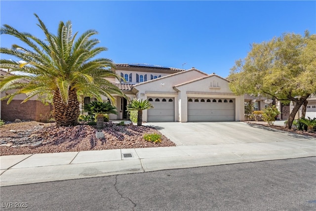 mediterranean / spanish-style home featuring a garage, concrete driveway, stucco siding, roof mounted solar panels, and a tile roof