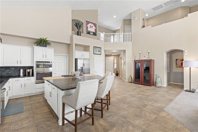 kitchen with stainless steel appliances, dark countertops, a kitchen breakfast bar, arched walkways, and white cabinetry