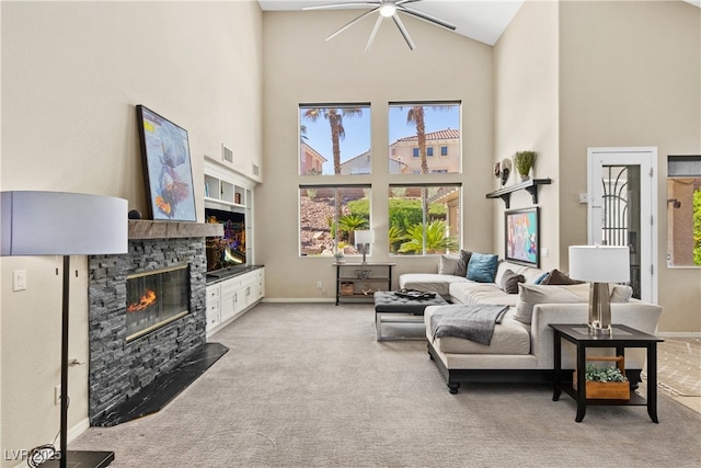 living area featuring a high ceiling, a fireplace, ceiling fan, light carpet, and plenty of natural light