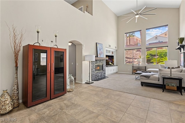living room featuring high vaulted ceiling, light colored carpet, arched walkways, light tile patterned flooring, and a stone fireplace