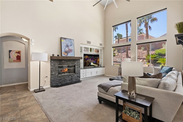 tiled living area with a high ceiling, a stone fireplace, a ceiling fan, baseboards, and arched walkways