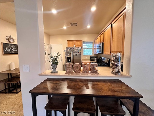 2558 Divine Sky Dr, Henderson, NV 89044 - kitchen with stainless steel appliances, light countertops, a peninsula, light tile patterned floors, and brown cabinetry