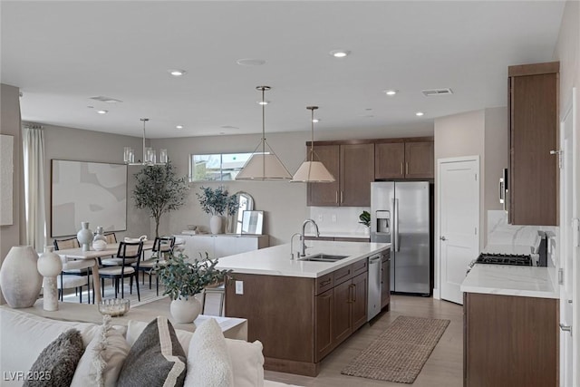 kitchen featuring appliances with stainless steel finishes, a sink, light countertops, dark brown cabinetry, and a kitchen island with sink