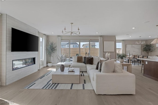 living room with a chandelier, a large fireplace, light wood-type flooring, healthy amount of natural light, and recessed lighting
