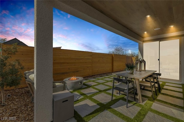 patio terrace at dusk featuring an outdoor fire pit, a fenced backyard, and outdoor dining space