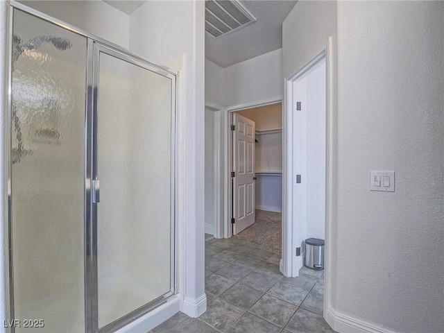 full bath with a shower stall, a walk in closet, a textured wall, baseboards, and tile patterned floors