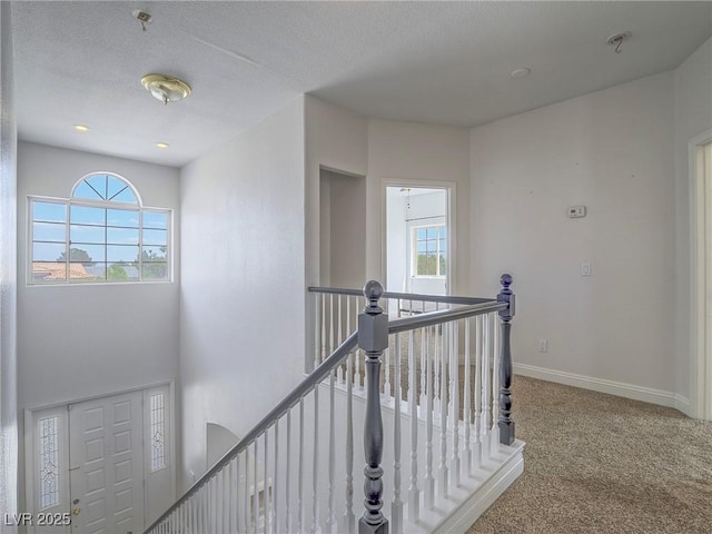 hallway with an upstairs landing, carpet floors, baseboards, and a textured ceiling