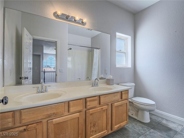 full bathroom with healthy amount of natural light, toilet, baseboards, a textured wall, and double vanity