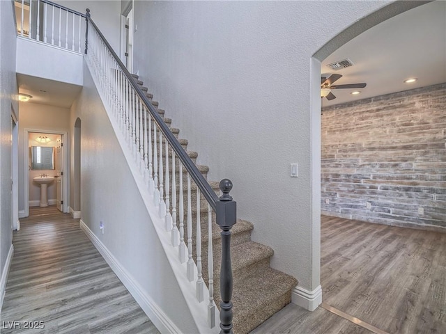 staircase with arched walkways, ceiling fan, baseboards, and wood finished floors
