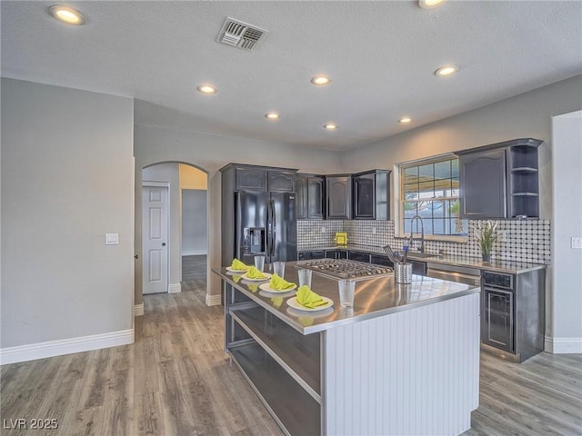 kitchen featuring open shelves, appliances with stainless steel finishes, arched walkways, a kitchen island, and light wood-type flooring