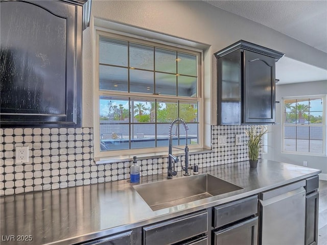 kitchen with stainless steel countertops, a sink, stainless steel dishwasher, and decorative backsplash