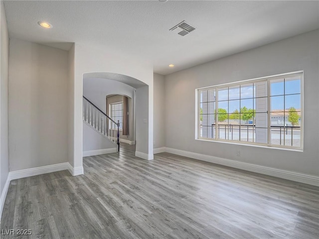 spare room with arched walkways, baseboards, wood finished floors, recessed lighting, and stairs