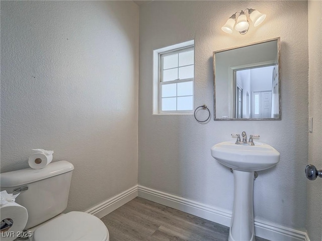 half bathroom featuring toilet, wood finished floors, and baseboards