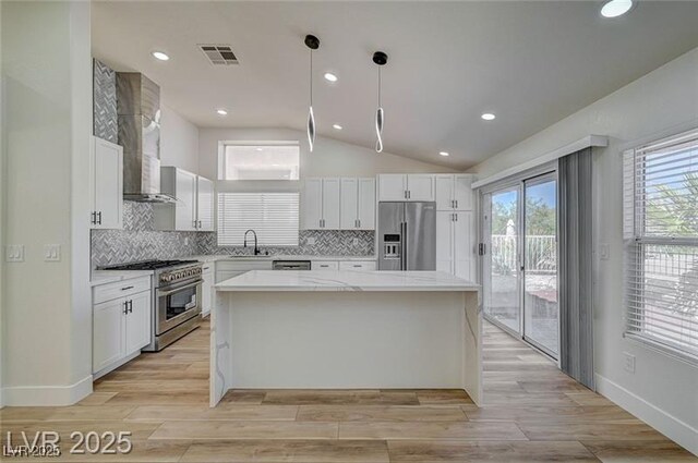 7460 Desert Flame Ct, Las Vegas, NV 89149 - kitchen with appliances with stainless steel finishes, vaulted ceiling, a sink, white cabinets, and wall chimney exhaust hood