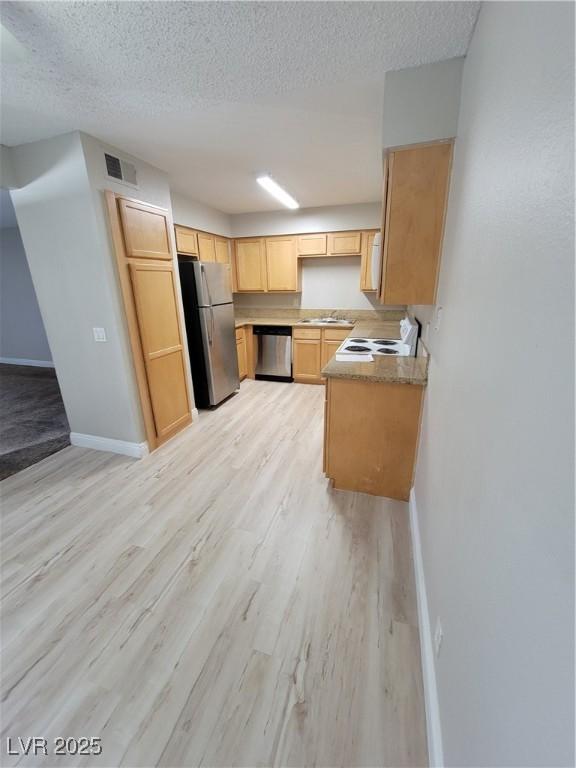 3151 Soaring Gulls Dr Unit 2101, Las Vegas, NV 89128 - kitchen featuring stainless steel appliances, light wood-style floors, baseboards, light brown cabinetry, and a textured ceiling