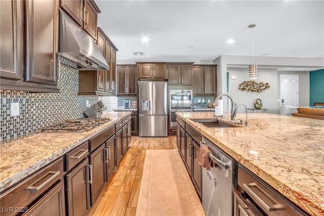 kitchen with stainless steel appliances, under cabinet range hood, a sink, light wood-type flooring, and light stone counters