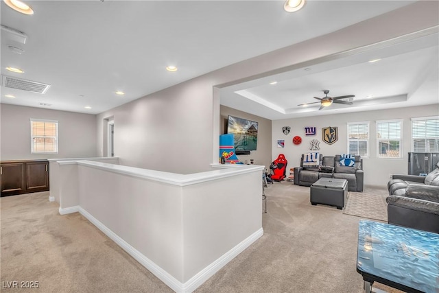 living area with light colored carpet, plenty of natural light, recessed lighting, and a tray ceiling