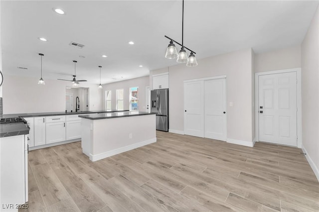 10345 Howling Coyote Ave, Las Vegas, NV 89135 - kitchen with stainless steel fridge with ice dispenser, dark countertops, a sink, white cabinets, and light wood-style flooring
