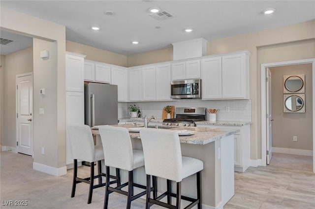 9903 Spinel Pl, Las Vegas, NV 89143 - kitchen with appliances with stainless steel finishes, a breakfast bar area, an island with sink, white cabinetry, and recessed lighting