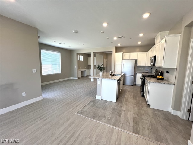 9903 Spinel Pl, Las Vegas, NV 89143 - kitchen featuring appliances with stainless steel finishes, open floor plan, a sink, an island with sink, and light stone countertops