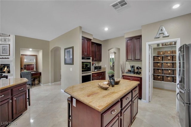 9046 Barium Rock Ave, Las Vegas, NV 89143 - kitchen featuring arched walkways, appliances with stainless steel finishes, dark brown cabinets, light stone counters, and a center island