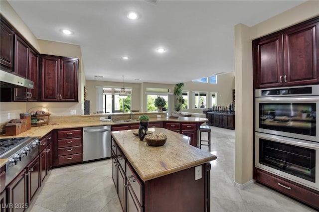 9046 Barium Rock Ave, Las Vegas, NV 89143 - kitchen featuring appliances with stainless steel finishes, reddish brown cabinets, a peninsula, under cabinet range hood, and a sink