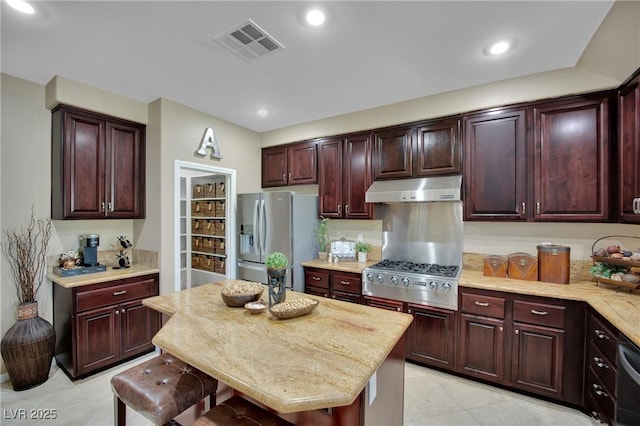 9046 Barium Rock Ave, Las Vegas, NV 89143 - kitchen featuring under cabinet range hood, stainless steel appliances, light tile patterned floors, reddish brown cabinets, and light stone counters
