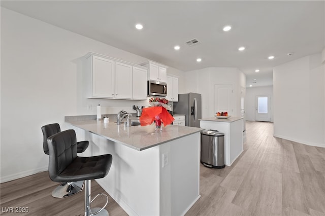 2729 Pavehawk Way, Las Vegas, NV 89156 - kitchen with stainless steel appliances, a center island, white cabinets, light wood-style flooring, and a peninsula