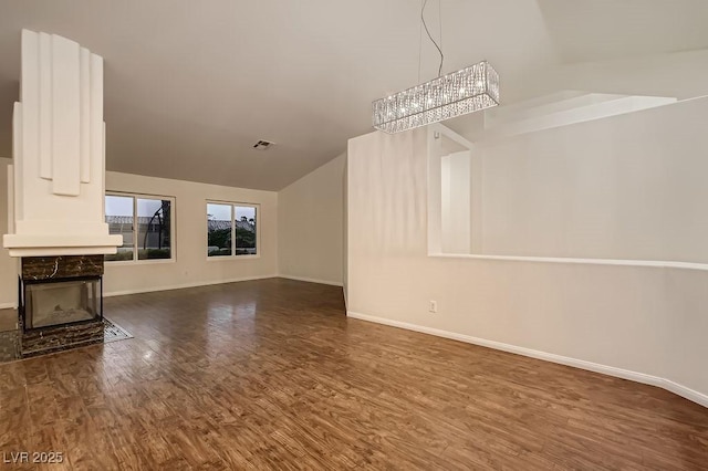 unfurnished living room featuring wood finished floors, baseboards, a chandelier, a high end fireplace, and vaulted ceiling