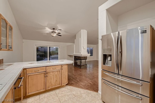 kitchen with stainless steel refrigerator with ice dispenser, tile counters, a ceiling fan, and glass insert cabinets