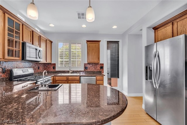 2432 Granada Bluff Ct, Las Vegas, NV 89135 - kitchen with stainless steel appliances, a sink, brown cabinetry, tasteful backsplash, and glass insert cabinets